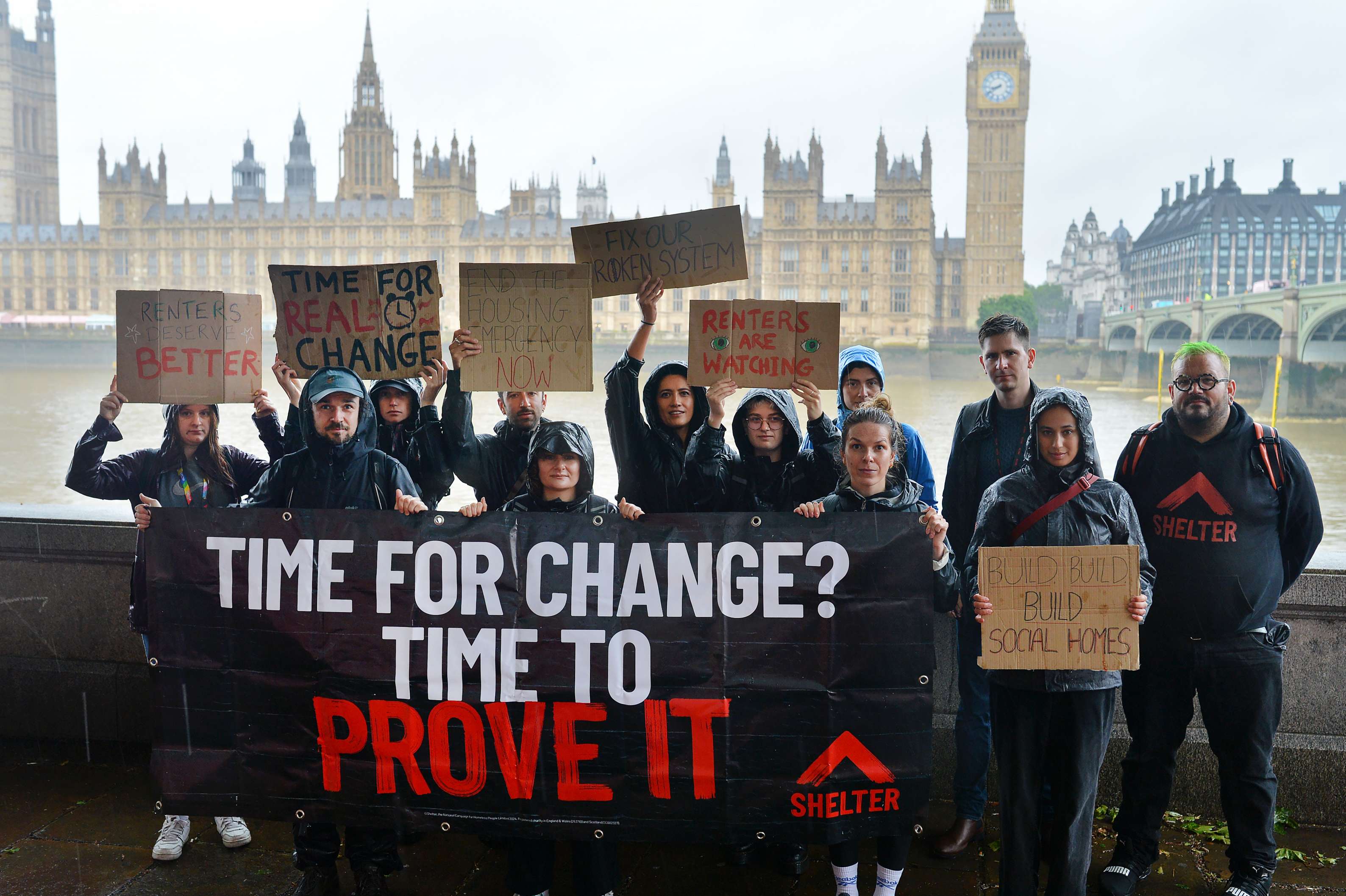 A group of Shelter campaigners stand with placards and a big banner in front of Westminster