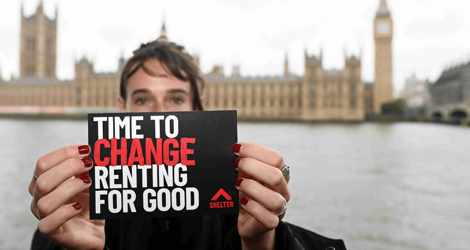 A person holds a postcard that reads 'Time to change renting for good'. They are stood in front of the river Thames, with parliament visible in the background.