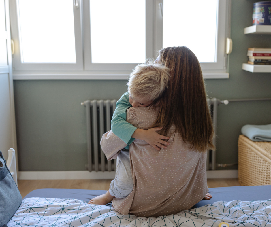 Person sitting on the edge of the bed holding their baby.