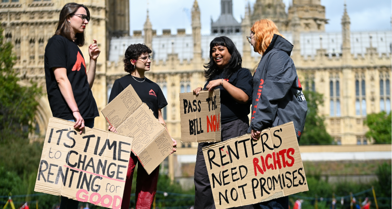 Someone holds a DIY placard over their face in Parliament Square. The sign reads 'Give Renters Rights' in orange and yellow paint.